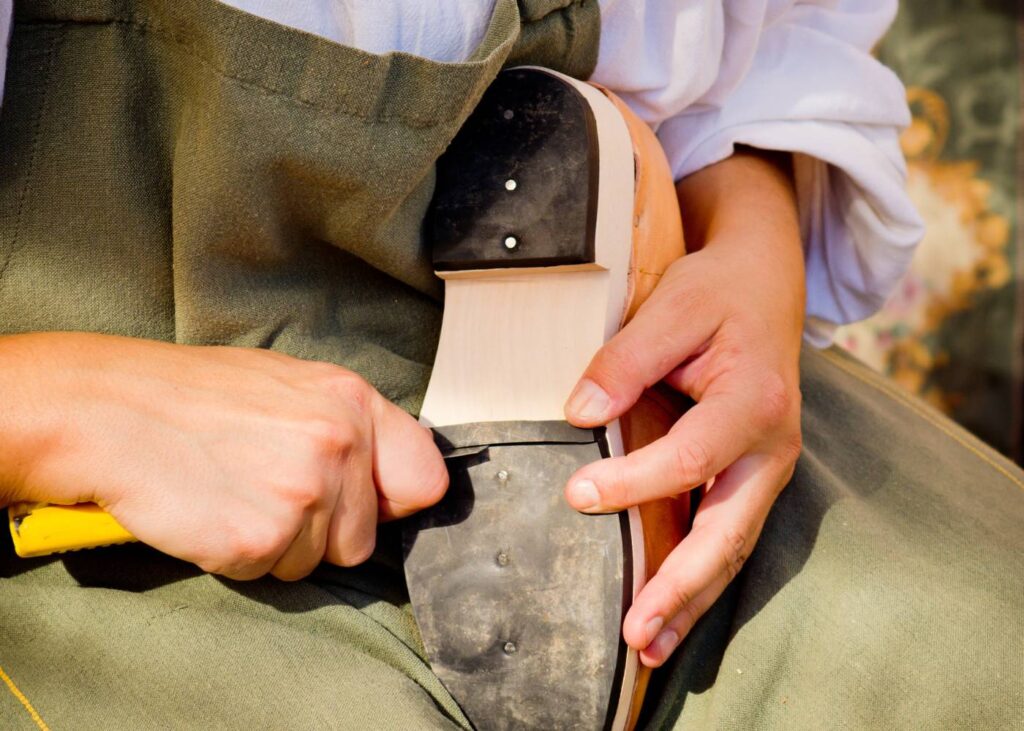 Na zdjęciu szec który naprawia but, trzyma w ręku scyzoryk